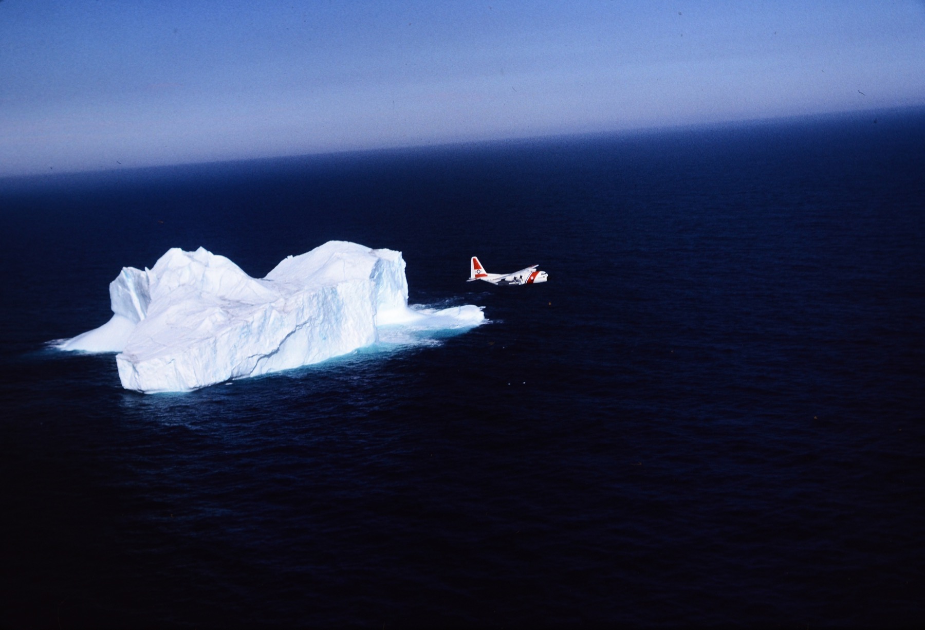 A U.S. Coast Guard C-130 aircraft flying past an iceberg near Newfoundland.