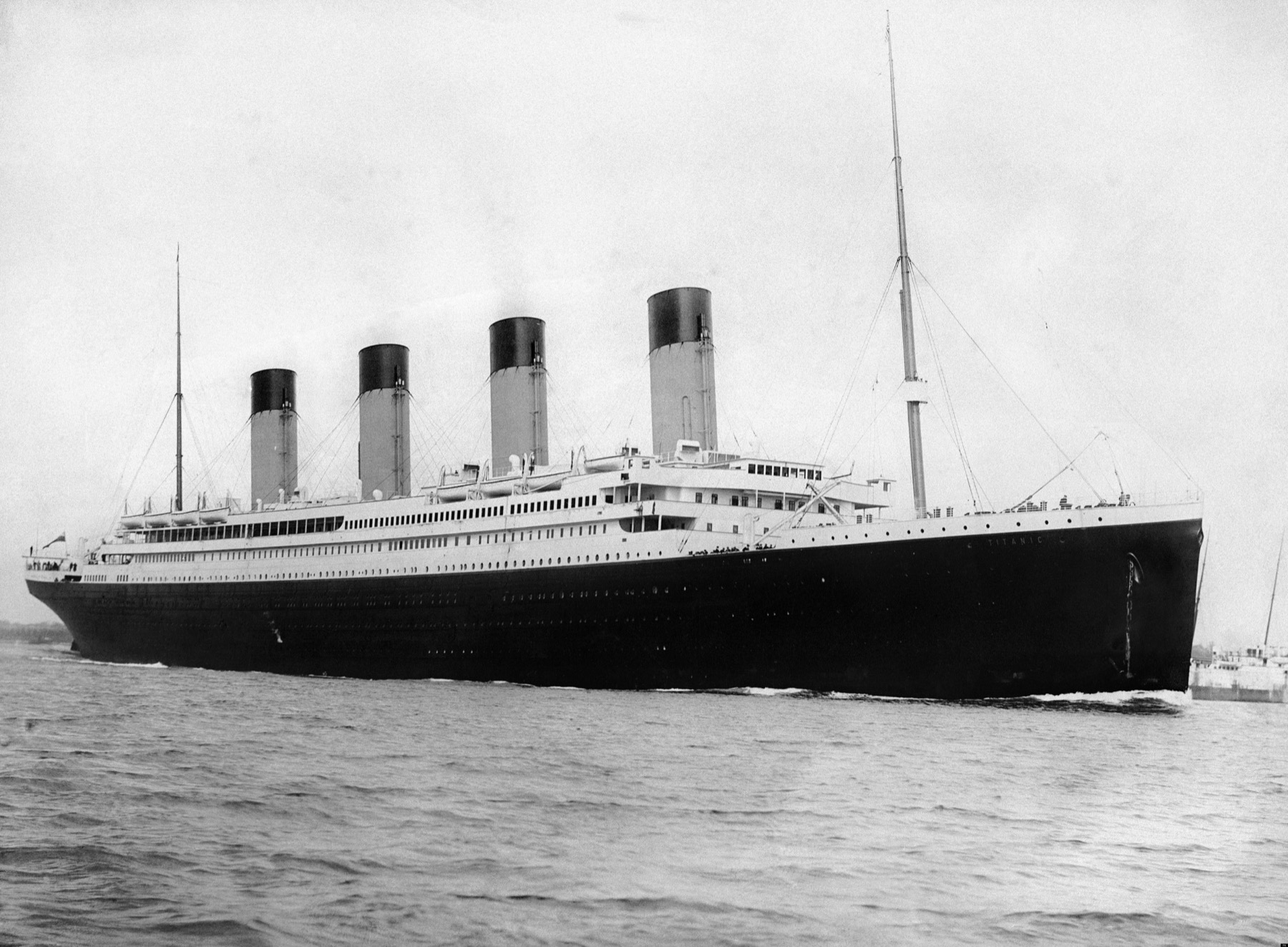 RMS Titanic departing Southampton with tugboats and people gathered along the quay.